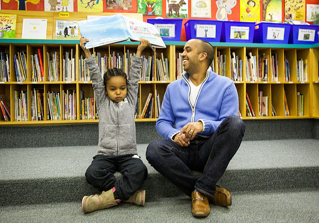 Neil Pasricha sitting in a library with a child who is holding up his book Awesome is Everywhere