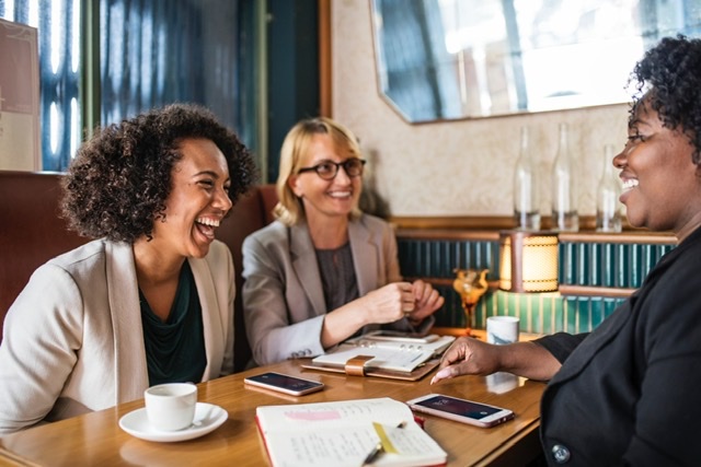 Three women laughing over coffee
